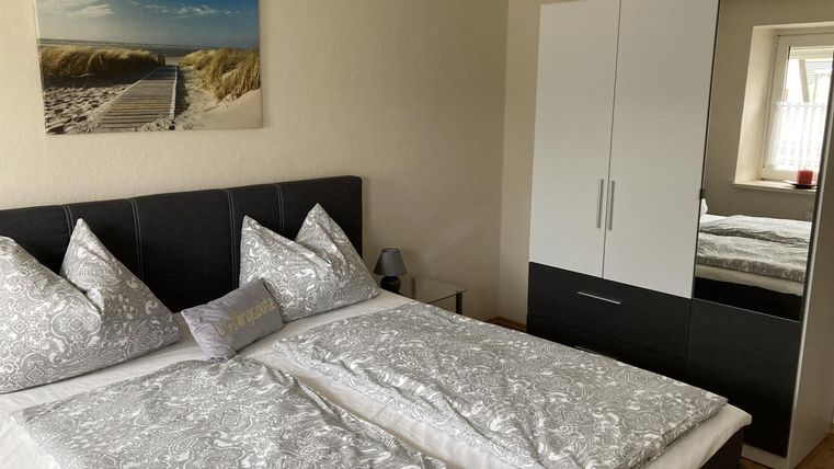 Een lichte slaapkamer met twee eenpersoonsbedden en moderne kussens. Op de achtergrond hangt een afbeelding van een strand en een grote kast staat tegen de muur.