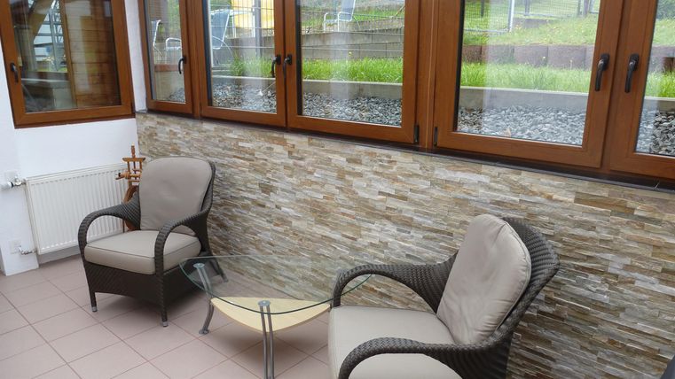 Ein gemütlicher Raum mit zwei Stühlen und einem kleinen Tisch. Die Wand ist mit Steinverkleidung und großen Fenstern ausgestattet.