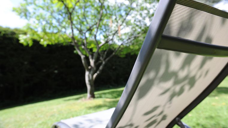 Eine Liege im Garten, umgeben von grünem Gras und einem Baum. Die Sonne scheint und sorgt für eine entspannte Atmosphäre.