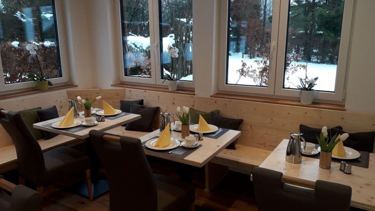 Ein gemütliches Restaurant mit Tischen, die für Gäste gedeckt sind. Durch die Fenster kann man schneebedeckte Landschaften sehen.