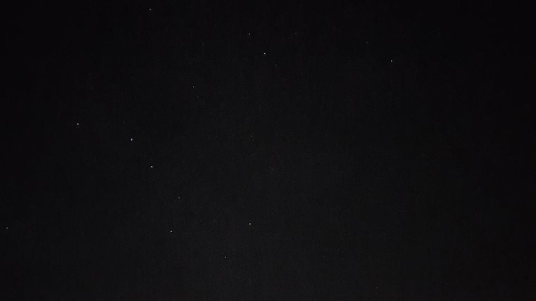 Ein dunkler Nachthimmel mit einigen leuchtenden Sternen. Im Vordergrund ist eine unscharfe Kontur eines Daches sichtbar.