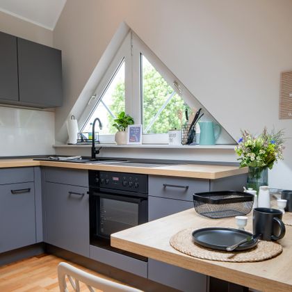 Een moderne keuken met schuine ramen en lichte muren. De tafel is gedekt en er staan verse bloemen als decoratie.