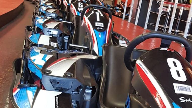A series of go-karts are lined up on a racetrack, ready. The vehicles are painted in blue-red colors and are numbered.