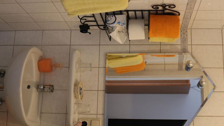 Ein helles Badezimmer mit weißen Fliesen und orangefarbenen Handtüchern. Ein Waschbecken und ein Spiegel sind gut sichtbar.