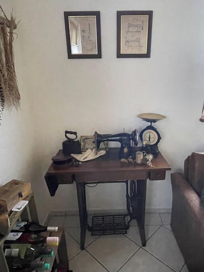 Een vintage naaimachine-tafel met verschillende gereedschappen en een oude weegschaal. Aan de muur hangen twee schilderijen.