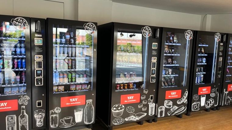 Een reeks snack- en drankautomaten in een lichte ruimte. De automaten zijn uitgerust met verschillende producten en een modern design.