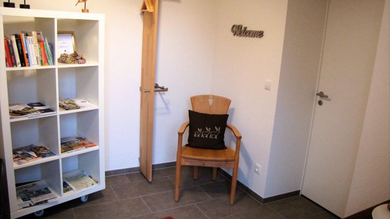 An inviting entrance area with a bookshelf and a chair. The walls are bright and modern, featuring a red carpet and a welcome sign.