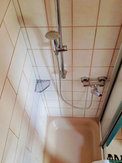 Een eenvoudige badkamer met een douche en tegels. De douchekraan en een douchekop zijn zichtbaar.