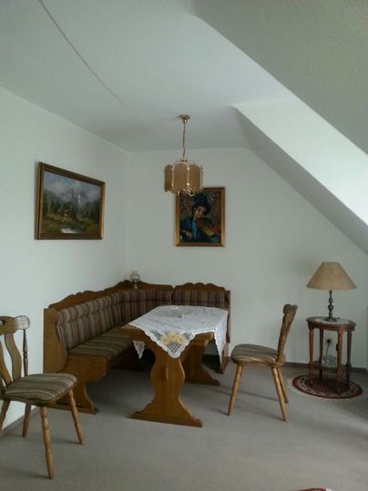 Ein gemütlicher Essbereich mit einem Holztisch und Bänken. An der Wand hängen zwei Bilder, und eine Lampe sorgt für Licht.