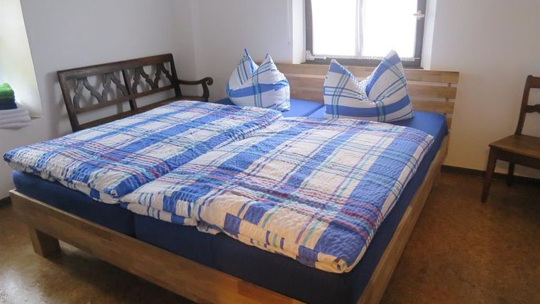 Een gezellige slaapkamer met een groot bed en blauwe geruite dekens. Twee kussens in de vorm van heuvels liggen op het bed, en een raam zorgt voor natuurlijk licht.