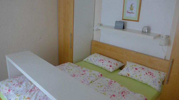 A simple bedroom with a double bed and colorful bedding. In the background, there is a wardrobe and a wall shelf.