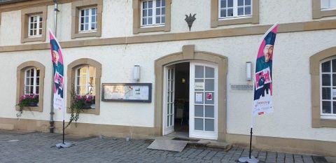 Een historisch gebouw met een uitnodigende ingang. Voor het gebouw staan twee vlaggen en plantenbakken met bloemen.