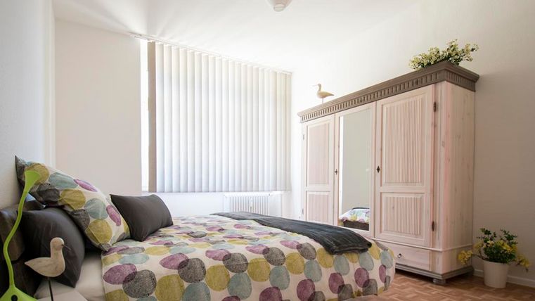 Ein helles Schlafzimmer mit einem Bett und buntem Bettzeug. Ein gemütlicher Kleiderschrank und eine dekorative Lampe ergänzen den Raum.