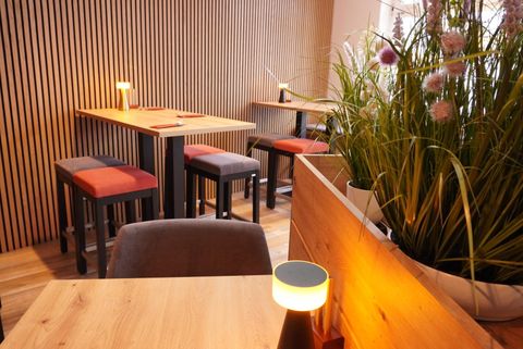 A modern restaurant with wood-paneled walls and stylish tables. Soft lighting and green plants create an inviting atmosphere.