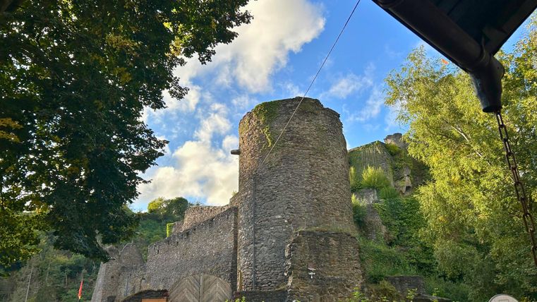 An old castle wall surrounded by trees and hills. The sky is partly cloudy and the light is soft.