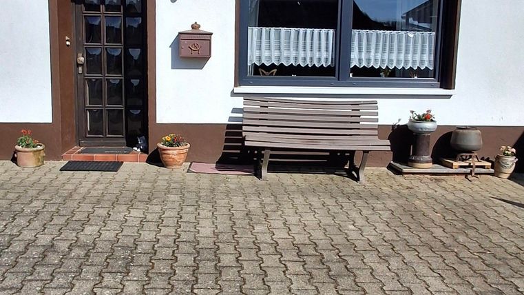 Ein modernes Haus mit einer weißen Fassade und braunen Fensterrahmen. Die Auffahrt ist gepflastert und es gibt eine Sitzbank vor der Haustür.