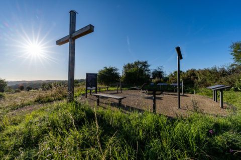 Ein schöner Aussichtspunkt mit einem Holzschild und Informationstafeln. Im Hintergrund strahlt die Sonne über einer grünen Wiese.