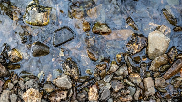A clear flow of water cascading over round stones. The various stones have different colors and textures.