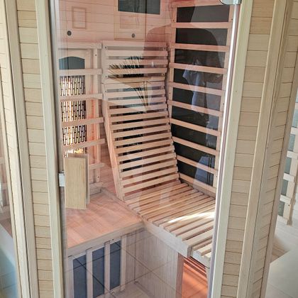 A modern sauna with a wooden interior and a comfortable lounging area. The sauna features a clear glass front and soft lighting.