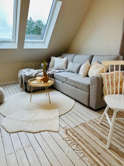 Een gezellige woonkamer met een grijze bank en grote ramen. De vloer is van hout en er ligt een zacht tapijt in de ruimte.