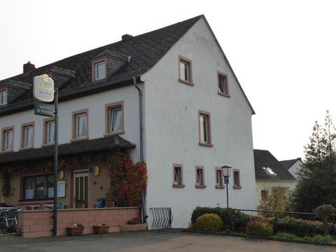 Ein zweigeschossiges Haus mit einem einfachen Äußeren und einem einladenden Eingangsbereich. Vor dem Haus sind kleine Blumenbeete und eine ruhige Straße zu sehen.