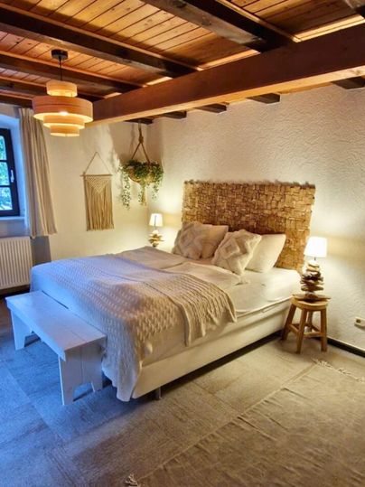 A cozy bedroom with a large bed and wooden ceiling. The room is warm and inviting, featuring a calm color palette and atmospheric lighting.