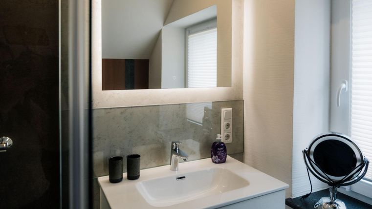 Ein modernes Badezimmer mit einem eleganten Waschbecken und einem großen Spiegel. Die Wände sind hell und es gibt dekorative Elemente wie Kerzen und einen Spiegel.