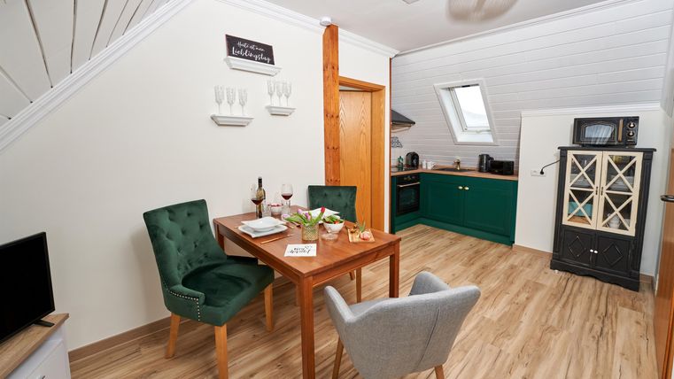 A cozy living kitchen with a dining table and two chairs. The walls are bright, and the kitchen has green accents.