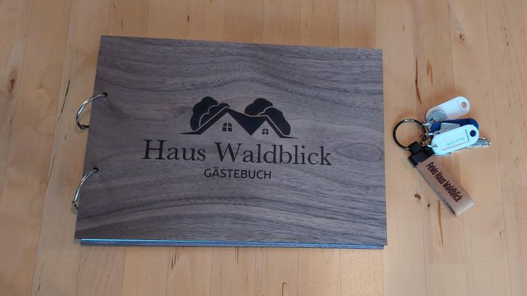 Ein Gästebuch mit dem Titel "Haus Waldblick" liegt auf einem Holztablett. Daneben befindet sich ein Schlüsselbund.