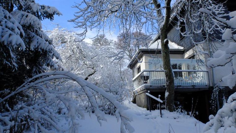Een besneeuwde tuin met een modern huis in het winterlandschap. De bomen zijn bedekt met sneeuw en de lucht is helder en blauw.