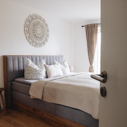 Ein modernes Schlafzimmer mit einem großen Bett und schönen Kissen. Es hat helle Wände und viel natürliches Licht, das durch ein Fenster strömt.