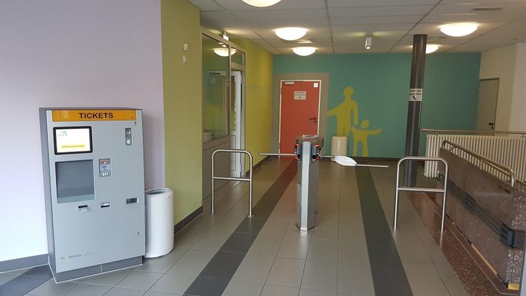 A modern entrance area with a ticket machine and automatic turnstiles. The walls are painted in different colors, creating an inviting impression.