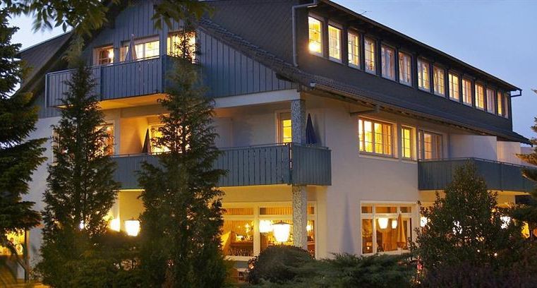 Ein modernes Hotelgebäude bei Dämmerlicht, umgeben von Bäumen. Die Lichter der Fenster schaffen eine einladende Atmosphäre.