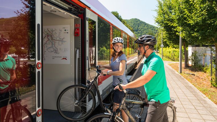 Two cyclists are boarding a train. A woman and a man are holding their bicycles and smiling.