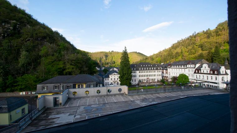 Eine malerische Landschaft mit Hügeln und Bäumen. Im Vordergrund sind Gebäude mit modernen und historischen Elementen zu sehen.