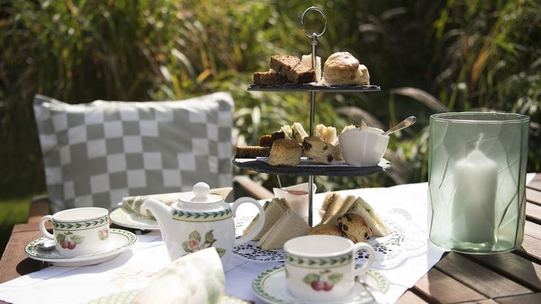 Een mooie middag koffie in de buitenlucht met een etagère vol lekkernijen. De kop en het servies zijn elegant en nodigen uit tot genieten.