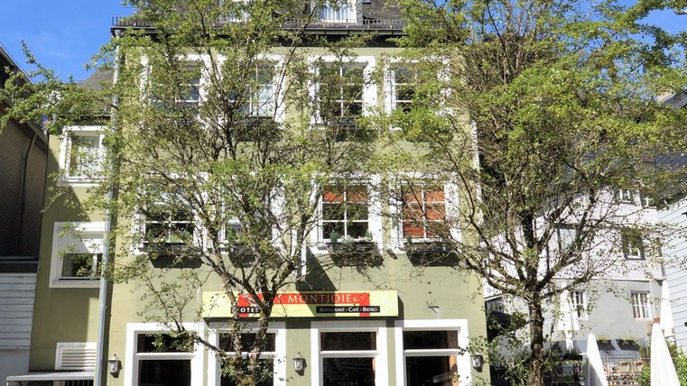 Ein charmantes Gebäude mit mehreren Fenstern und Pflanzen im Vordergrund. Es steht in einer lebhaften Straße unter klarem Himmel.