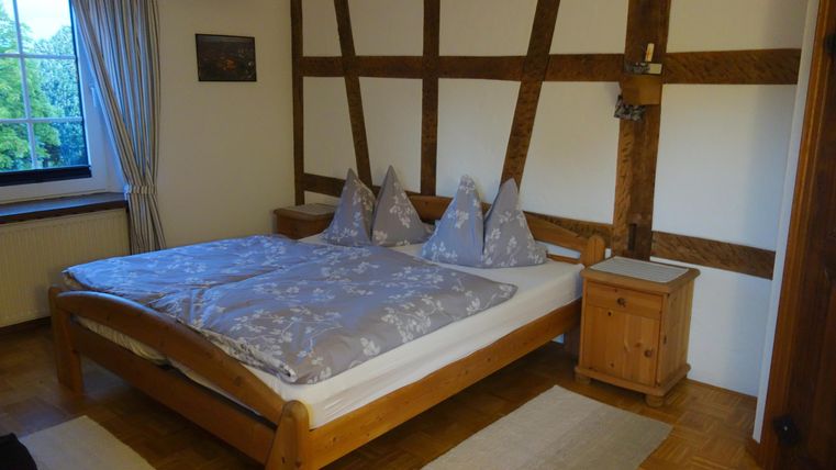 Een gezellig slaapkamer met een groot bed en houten meubels. De muren zijn in rustieke stijl met zichtbare balken vormgegeven.