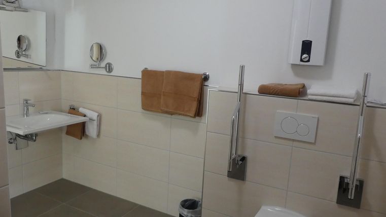 Ein modernes Badezimmer mit hellen Fliesen und handtüchern. Die Wände sind in neutralen Farben gehalten, und es gibt einen Spiegel über dem Waschbecken.