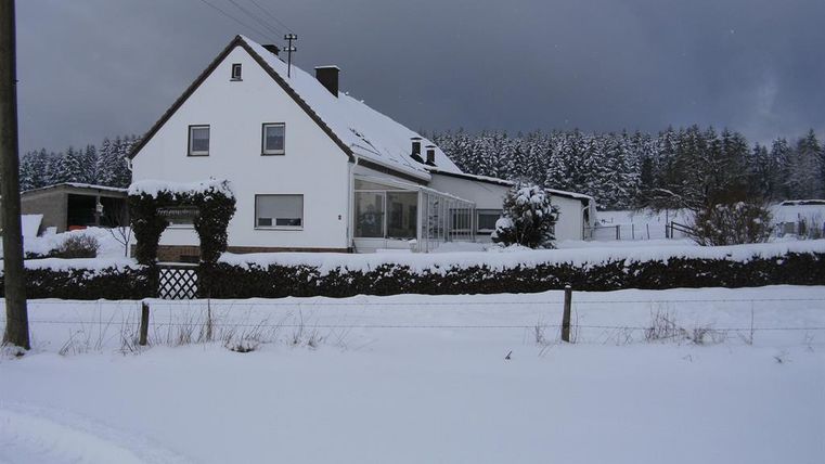 Ein schönes Haus im Schnee, umgeben von einem winterlichen Landschaft. Der Himmel ist grau und es gibt viele schneebedeckte Bäume in der Nähe.