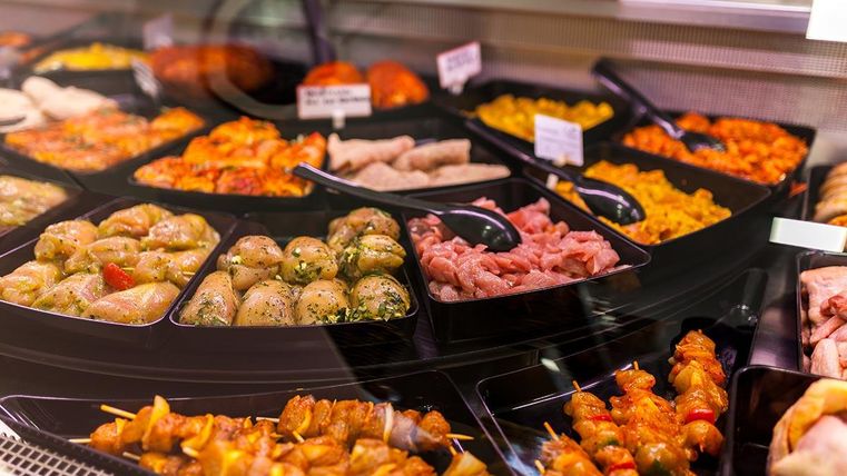 Een grote selectie van heerlijk eten in containers. Er zijn vleesspiezen, gevulde deegwaren en kleurrijke bijgerechten.