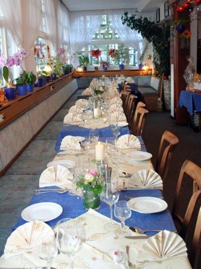 Ein festlich gedeckter Tisch mit blauen Tischdecken und dekorativen Servietten. Der Raum ist hell mit Pflanzen und Blumen dekoriert.