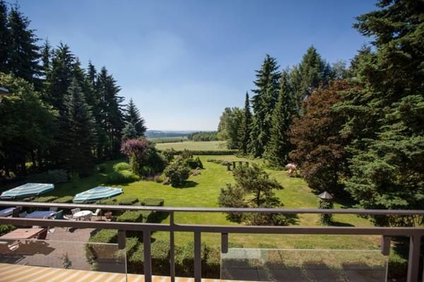 Een mooie tuin met goed onderhouden gazons en hoge bomen. Op de achtergrond is een uitgestrekte landschap te zien onder een heldere lucht.
