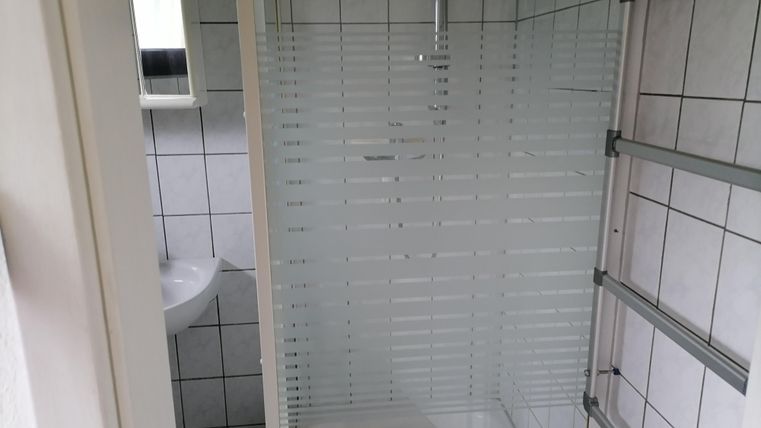 Een moderne badkamer met een douchecabine en betegelde wanden. Op de achtergrond bevindt zich een klein wastafel en een spiegel.