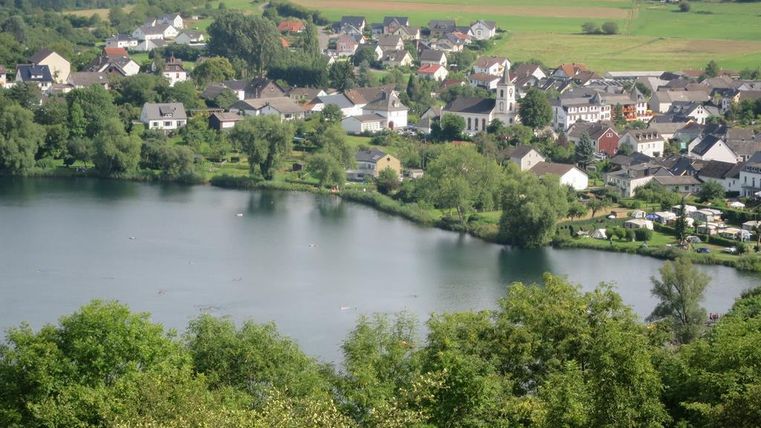 Een schilderachtig landschap met een rustige Meer en omliggende huizen. Groene bomen en weilanden voltooien de idyllische scène.