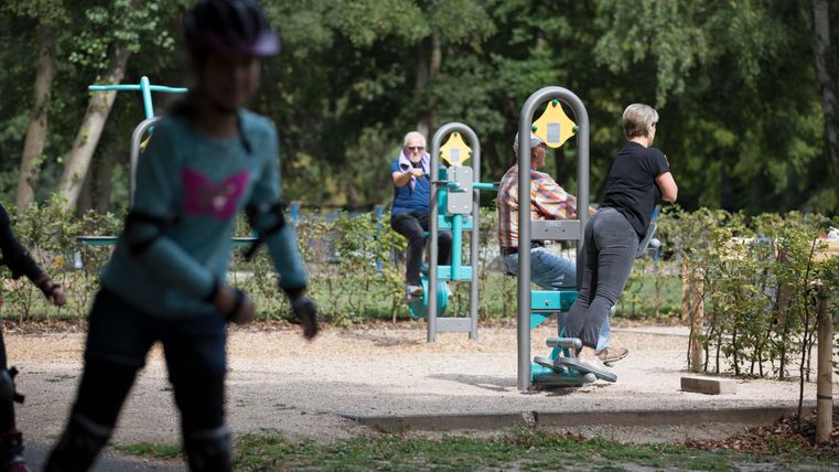 A beautiful playground with fitness equipment and various activities.
Children are rollerblading nearby while adults use the equipment.