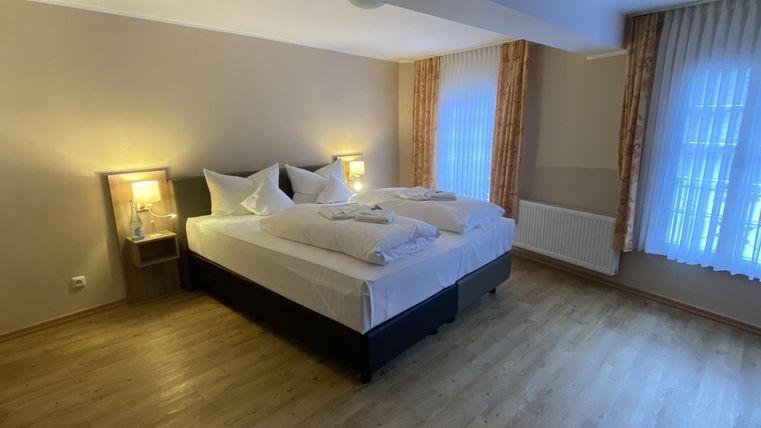 Ein gemütliches Schlafzimmer mit einem großen Doppelbett und hellen Vorhängen. Die warmen Lichter schaffen eine einladende Atmosphäre.