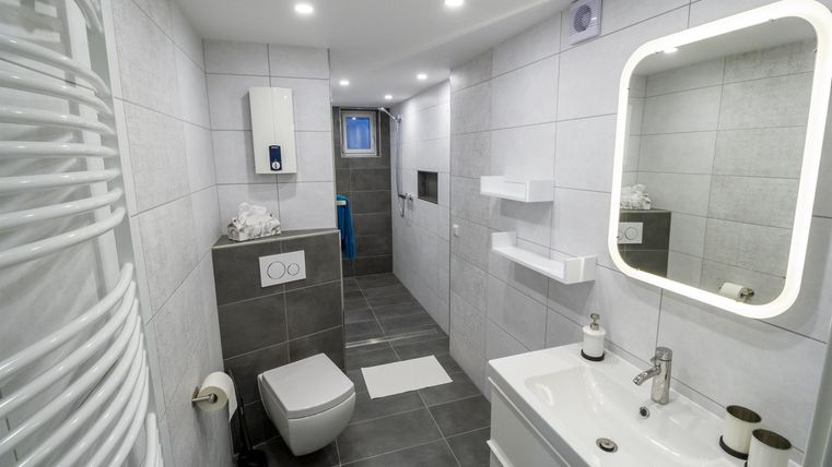 A modern bathroom with white tiles and elegant furniture. There is a shower, a sink, and a toilet.