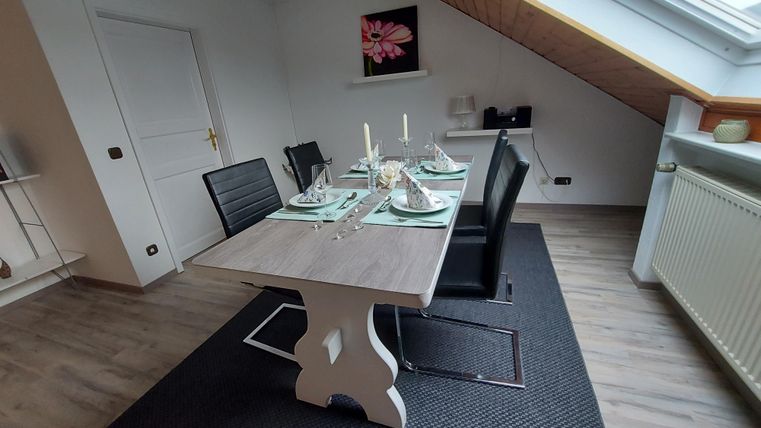 A modern dining area with a table and black chairs. The room has a cozy atmosphere with plenty of natural light and understated decoration.