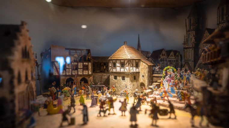 A detailed miniature scene featuring a village and figures that create a festive atmosphere. The image depicts historic buildings and cheerful people amidst activities.